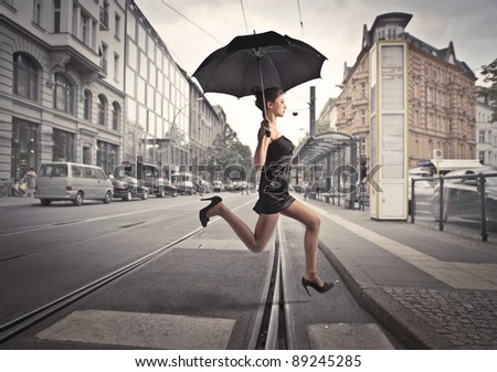 Beautiful woman running under an umbrella on a city street