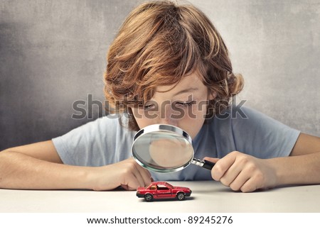 Child observing a toy-car through a magnifying glass