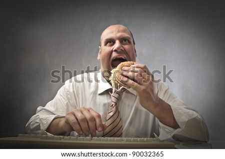Fat businessman eating a hamburger while using a computer