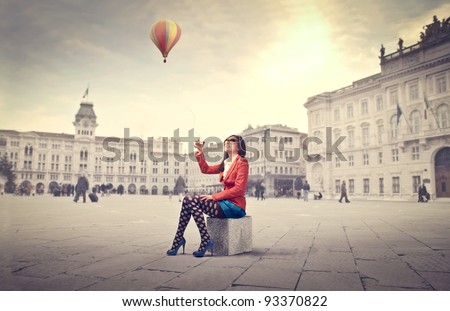 Beautiful woman in colored clothes on a square with hot-air balloon in the background