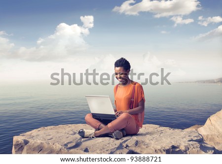 Smiling african woman using a laptop with seascape in the background