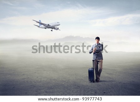 Businessman with trolley case looking at his watch with airplane in the background