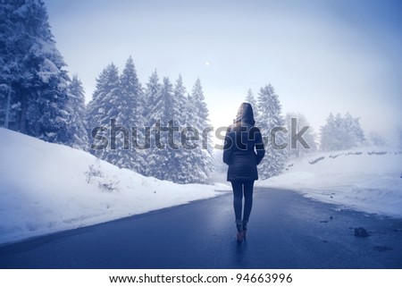 Woman in winter clothes walking on a road surrounded by snow