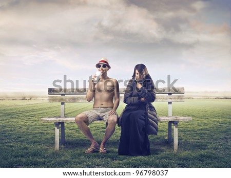 Man in summer clothes sitting on a park bench with woman wrapped in warm clothes beside him