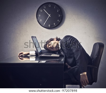 Tired businessman sleeping on a laptop with clock in the background