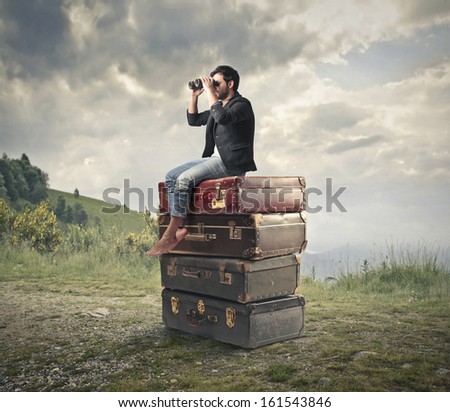 young man sitting on a pile of vintage suitcases looking with binoculars the panorama