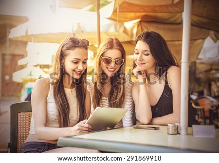 Three girls at the cafe staring at a tablet Three girls at the cafe staring at a tablet