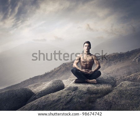 Handsome bare-chested young man doing yoga on a rock