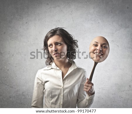 Young woman with sad expression holding a mask expressing cheerfulness - stock photo