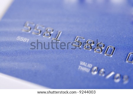 A blue credit card shot at an angle with the plane of focus being on the numbers. Numbers are fake.