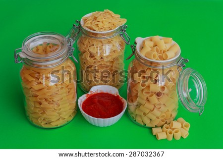 different sizes of pasta to choose from confined in glass jars with bowl of red sauce