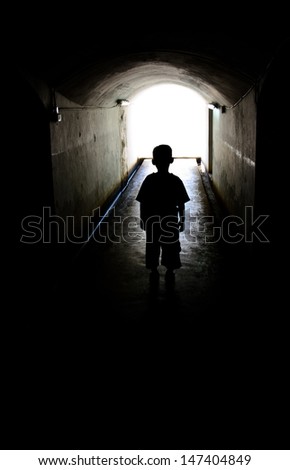 young boy in long tunnel walkway with the white light at the end