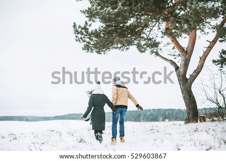 Young couple running on a snowy winter field near a big old pine