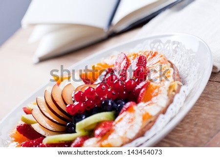 Delicious Fruit Tart. View of a delicious Fruit Tart placed in a dish on a wooden table and in the background a notepad for recipes