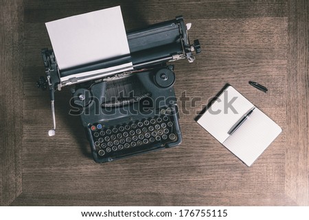 Top view of an old typewriter with a pen and a notebook on a wooden table, photo in retro style