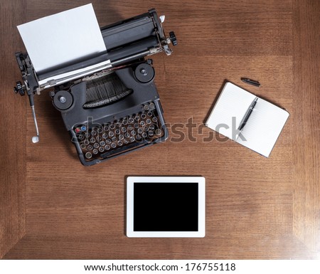 Top view of an old typewriter with a pen, a notebook and a tablet on a wooden table