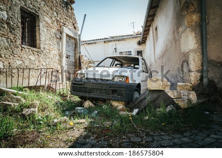 Years after the event of an earthquake, a car covered with rubble near the destroyed houses.