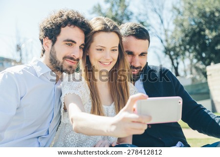 Selfie. On a sunny spring day, a group of three friends, two guys and a girl taking a photo of the park in a relaxing time.