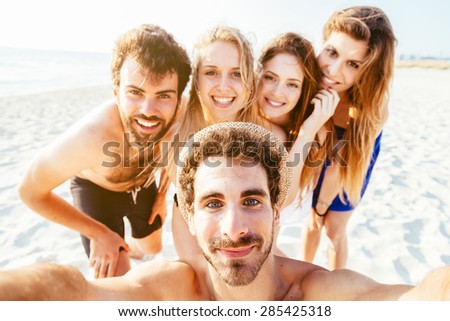 Selfie on the beach! Five friends in swimwear (two men and three women) take a photo with at the sea in a summer day at sunset on the beach with no other people