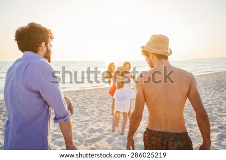 A group of friends, two men and three women, meets and embraces on the beach at sunset. The three friends to embrace the happiness of being. Sunset over the sea, sandy beach