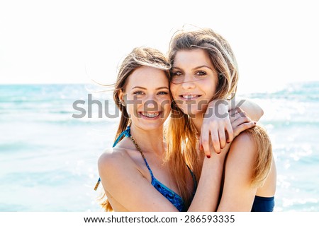Beach in summer. A couple of young women in swimwear hugging affectionately in the sun on a summer day. Close-up photo of the smiling faces