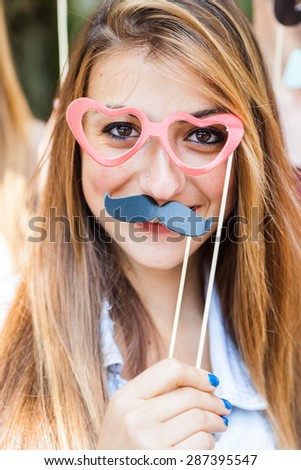 Party! A young blond woman at a party with friends in a park having fun wearing glasses and fake mustache