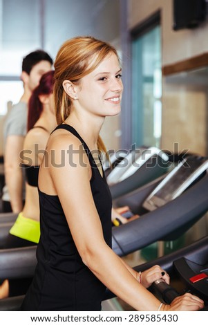 In a gym with other guys a beautiful blonde woman trains running on tapis rulant during a workout to stay in shape