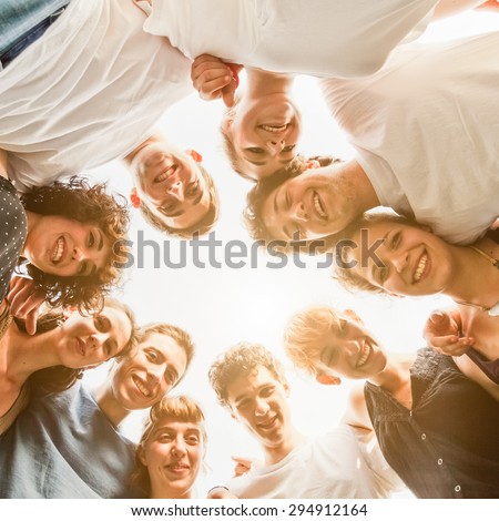 Group of ten young teenagers friends gathered to form a circle in the park, embraced each other. Group seen from bottom to top, during a summer day in a park at sunset