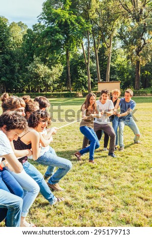 A group of ten teenage friends in a day of summer break from school, their fun at the park playing together tug of rope in a park