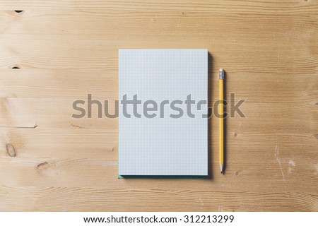 A recycled paper notebook checked with a black pencil with the eraser at the top, are arranged on a brown wooden table. View from the top