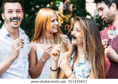Party! A group of friends, two women and two man have fun at a party in a park with a mustache and fake glasses, joking and talking to each other and playing