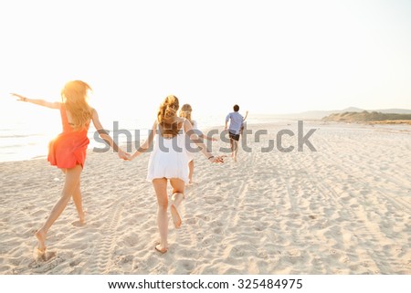 A group of friends runs on the deserted beach at sunset in the direction of the sunset. The last hours of day on the beach to have fun during the summer a group of teenagers. Two friends holding hands