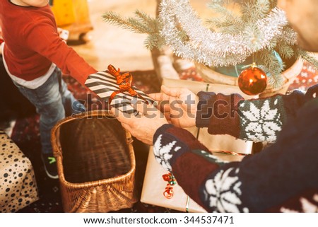 A blond haired toddler and her family exchanging Christmas gifts near the Christmas tree on Christmas Day to celebrate the event. The child takes with the hand the gift his father gives him