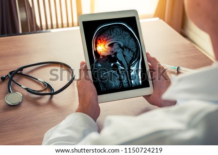 Doctor holding a digital tablet with x-ray of brain and skull skeleton. Headache, meningitis and migraine concept with stethoscope and syringe on the desk