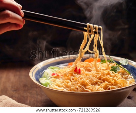 Hand uses chopsticks to pickup tasty noodles with smokes, dark background