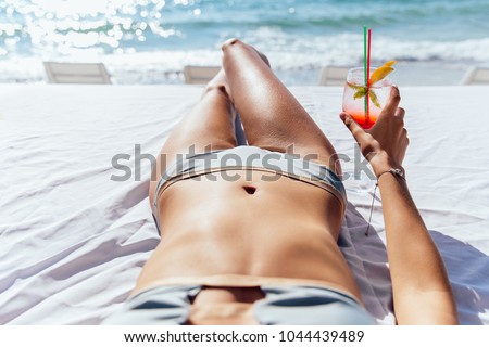 Woman with cocktail takes a sunbathe on sunbed, near the sea. Close-up view.
