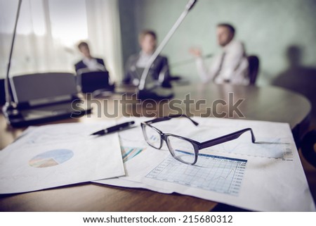 financial chart near dollars seen by unfocused glasses ( colleagues meeting to discuss their future financial plans only silhouettes being viewed )