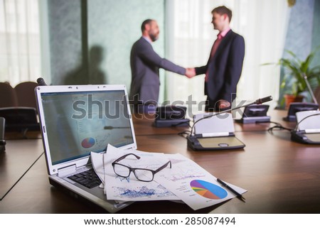 financial chart near dollars seen by unfocused glasses ( colleagues meeting to discuss their future financial plans only silhouettes being viewed ) \
two businessmen shake hands