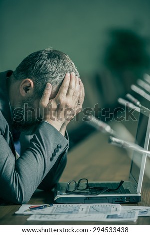 businessman with a big beard in a panic and depression has her head  	\
on the backdrop of the conference hall in the green range