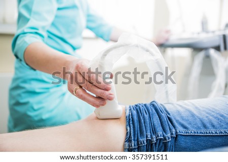 closeup hand of woman doctor doing an ultrasound of the legs of a man and knee