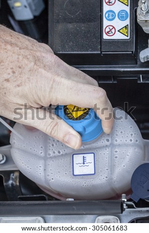 Hand checking the top of the cooling fluid reservoir in a car engine