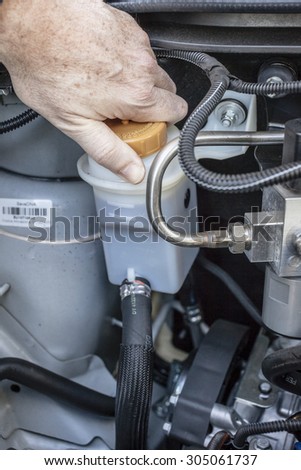Hand checking the top of the brake fluid reservoir in a car engine