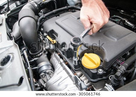 Hands repairing a car engine with a wrench