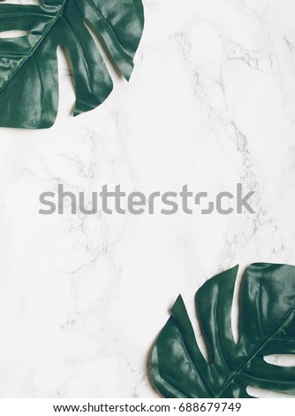 Big green tropical leaves on white marble background. Flat lay. Top view. Copy space.