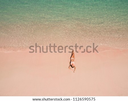 Top aerial view of a woman on the beach in a bikini lying and sunbathing on pink beach. Pink Beach, Padar Island, Komodo Flores, Indonesia