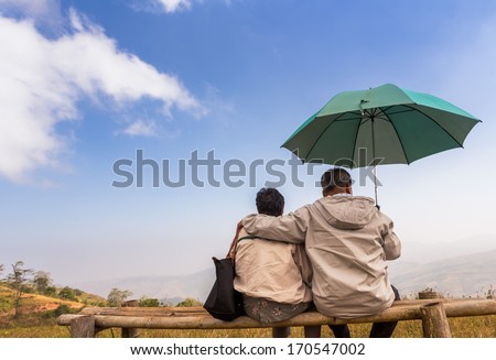 Old couple husband and wife sitting embrace and  looking view on top of the mountain