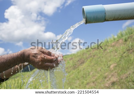 cleaning hands under an outdoor pipe pouring water. sky and cloud background