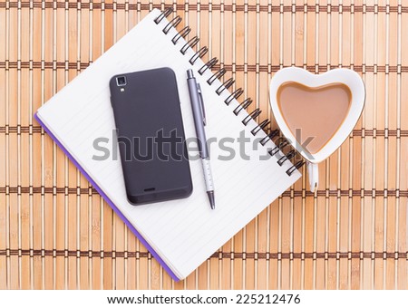 heart shaped  coffee  cup with smathphone ,pen and note book  on bamboo table cloth .view from above