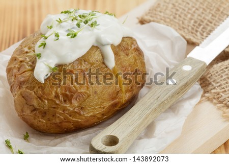 Baked potato with sour cream on wooden board