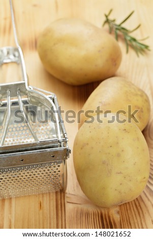 Potato masher and raw potatoes on wooden board